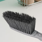 Woman using the long-handle cleaning brush for scrubbing a kitchen sink.