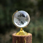 Elegant Crystal World Globe with golden stand, displayed next to a book and pen for desk decor.